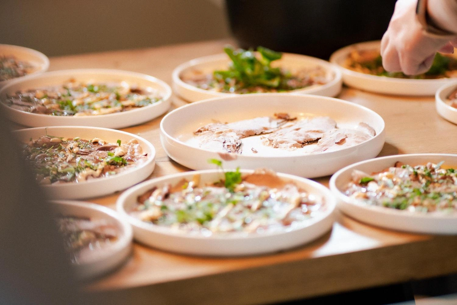 Mehrere weiße Teller mit kunstvoll angerichteten Speisen und frischen Kräutern auf einem Holztisch, bereit zum Servieren.