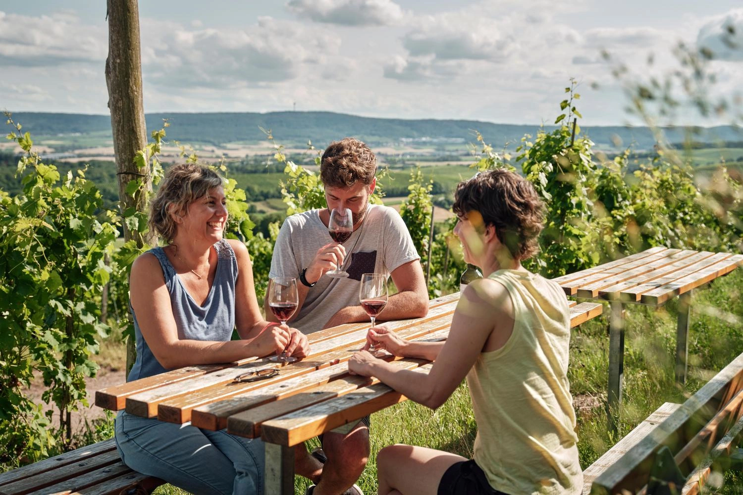 Zwei Frauen und ein Mann sitzen an einem Tisch in den Weinbergen und trinken Rotwein.