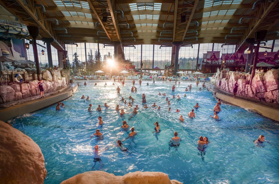 Many people are in a large indoor pool with a rocky backdrop; the scene conveys the fun and adventure on offer at the Rulantica water world at Europa-Park.
