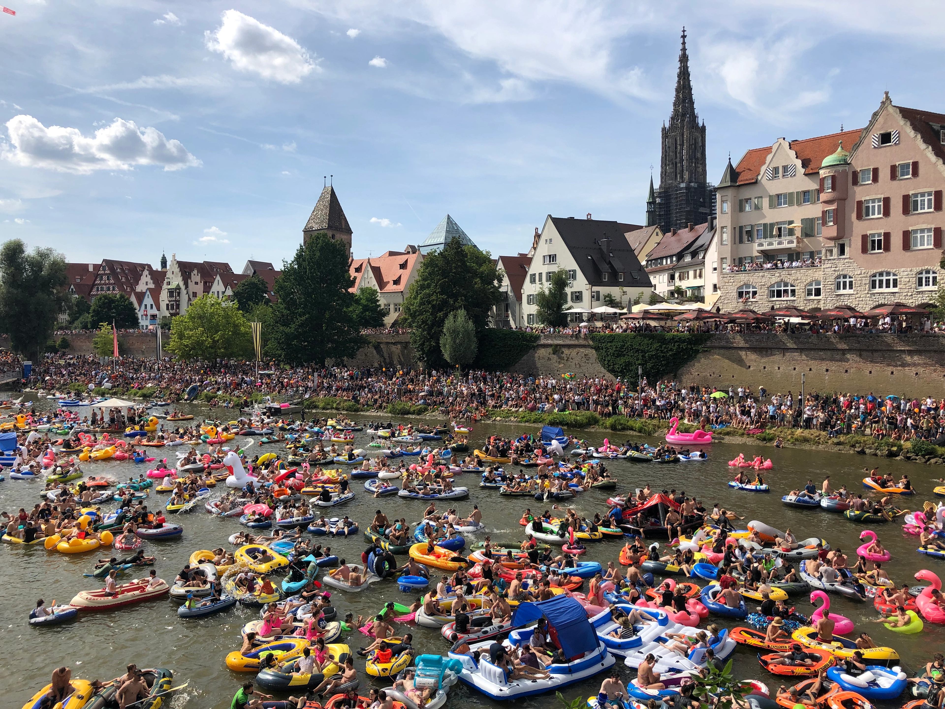 Hunderte bunte Schlauchboote und Menschen auf der Donau während des Nabada am Schwörmontag vor der Ulmer Altstadtkulisse mit dem Münster.