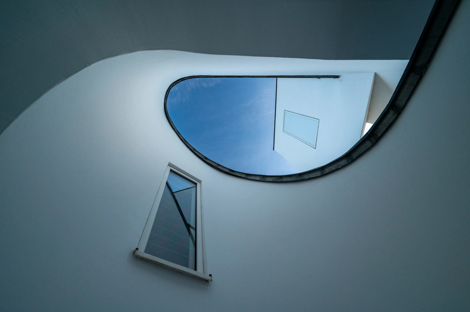 Blick Richtung Himmel aus dem Innenhof eines Gebäudes. Rundrum sind weiße Wände zu sehen und geschwungende Formen des Gebäudes.