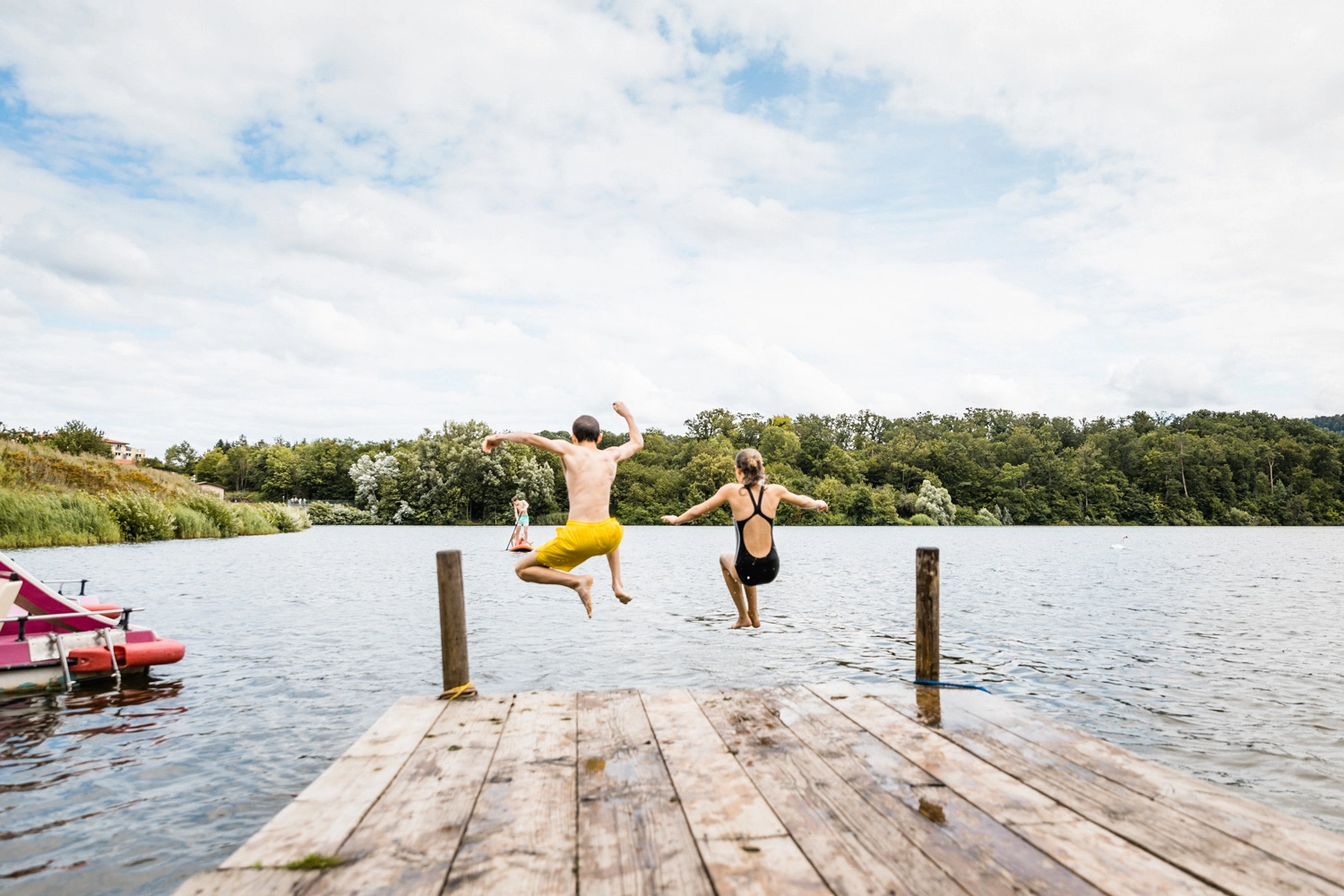 Ein Junge und ein Mädchen springen von einem Holzsteg ins Wasser.