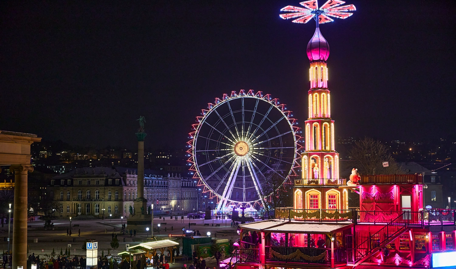 An illuminated pyramid and a Ferris wheel at night.
