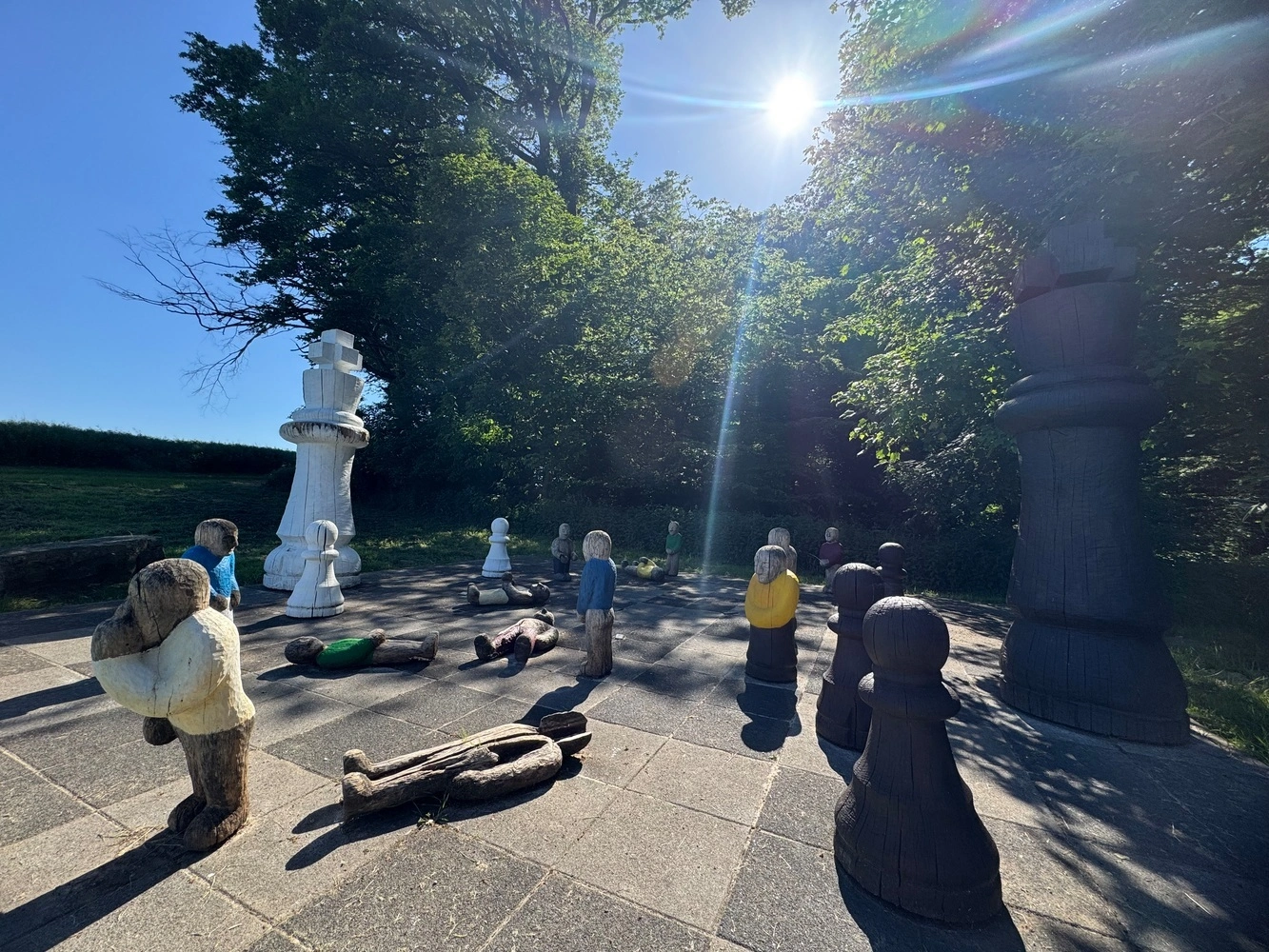 Übergroße hölzerne Schachfiguren stehen und liegen als Kunstinstallation auf einem Schachfeld.