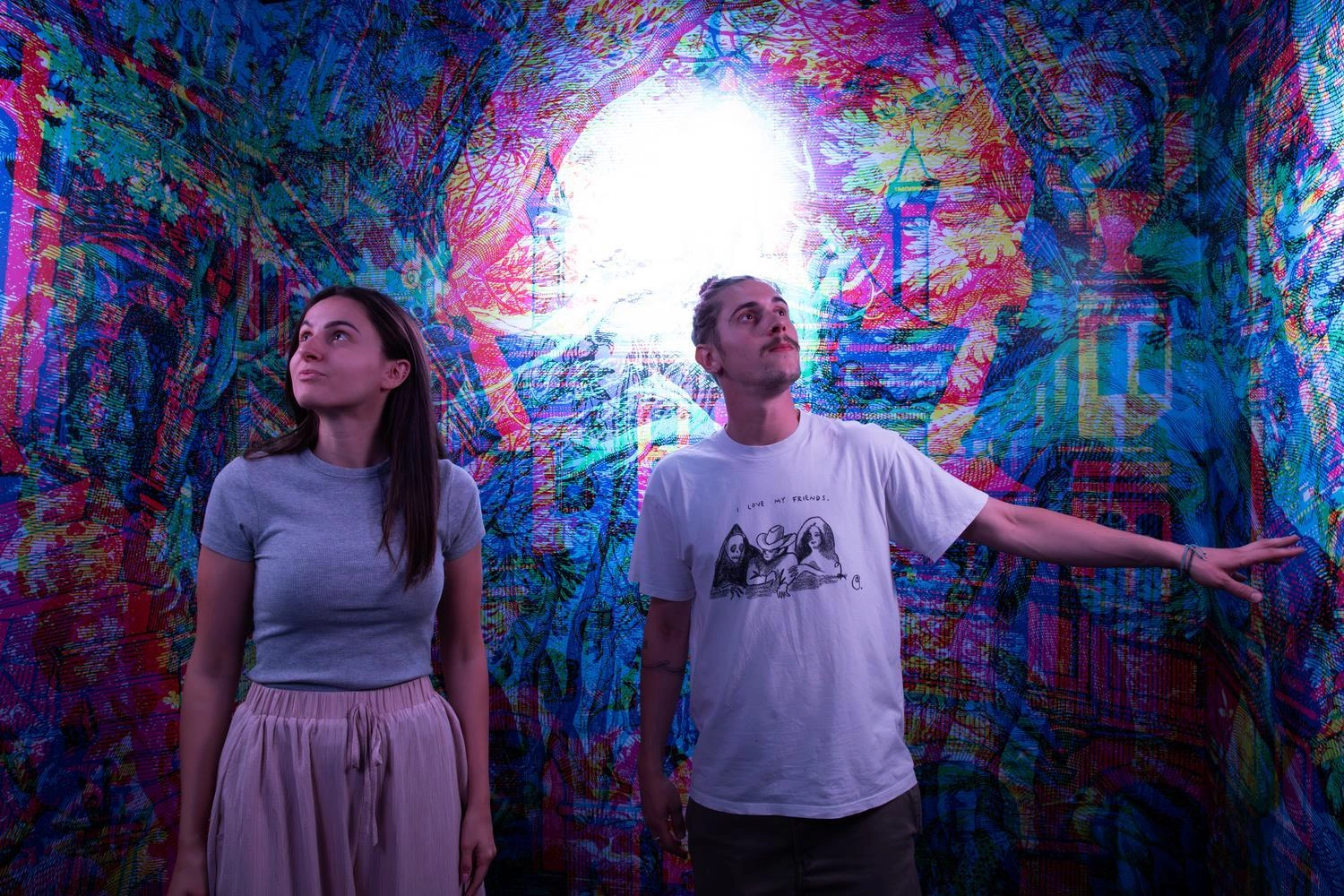 Zwei Personen stehen in einem Raum mit leuchtend bunten, psychedelischen Mustern und einem hellen Licht im Hintergrund,