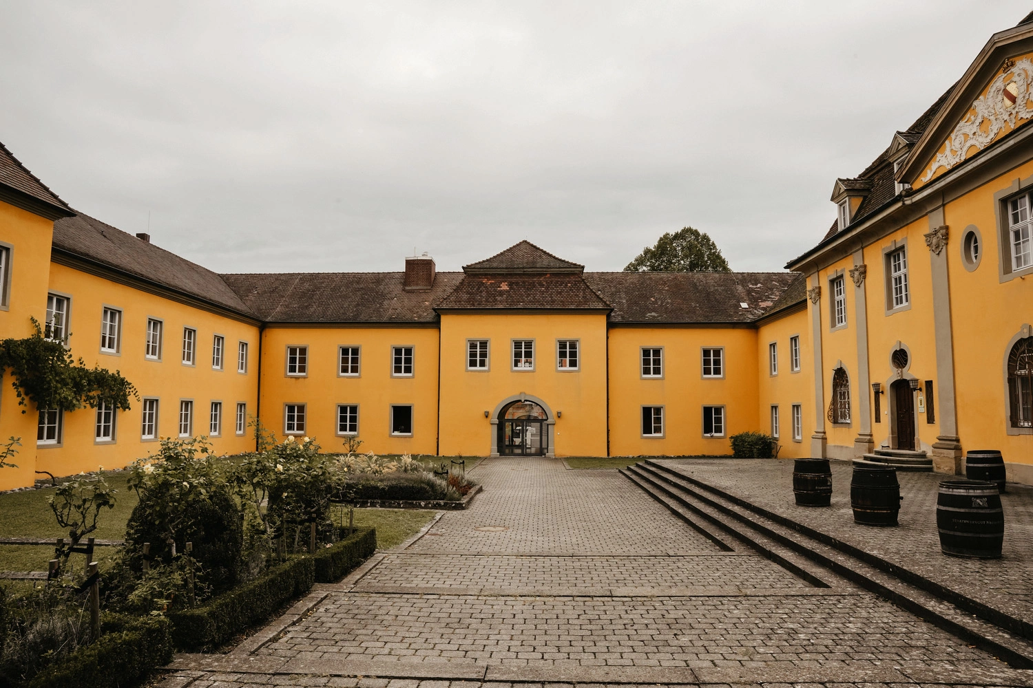 Blick auf ein U-förmiges, großes, gelbes Gebäude und einen gepflasterten Zugang
