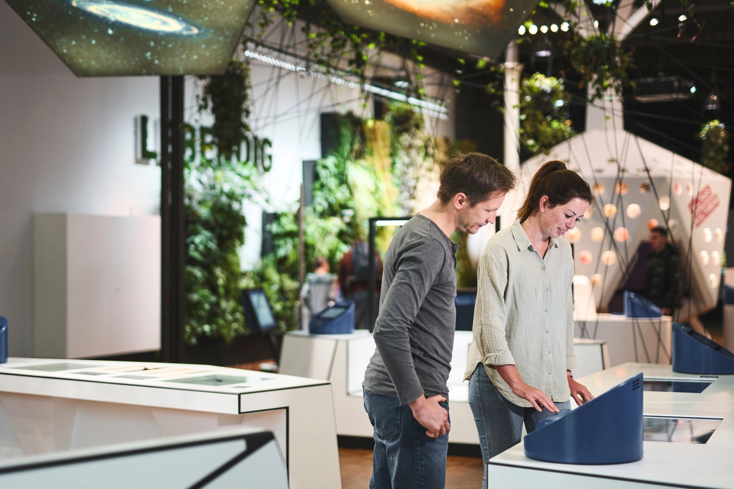 Visitors explore interactive stations in a modern exhibition featuring living walls and digital exhibits.
