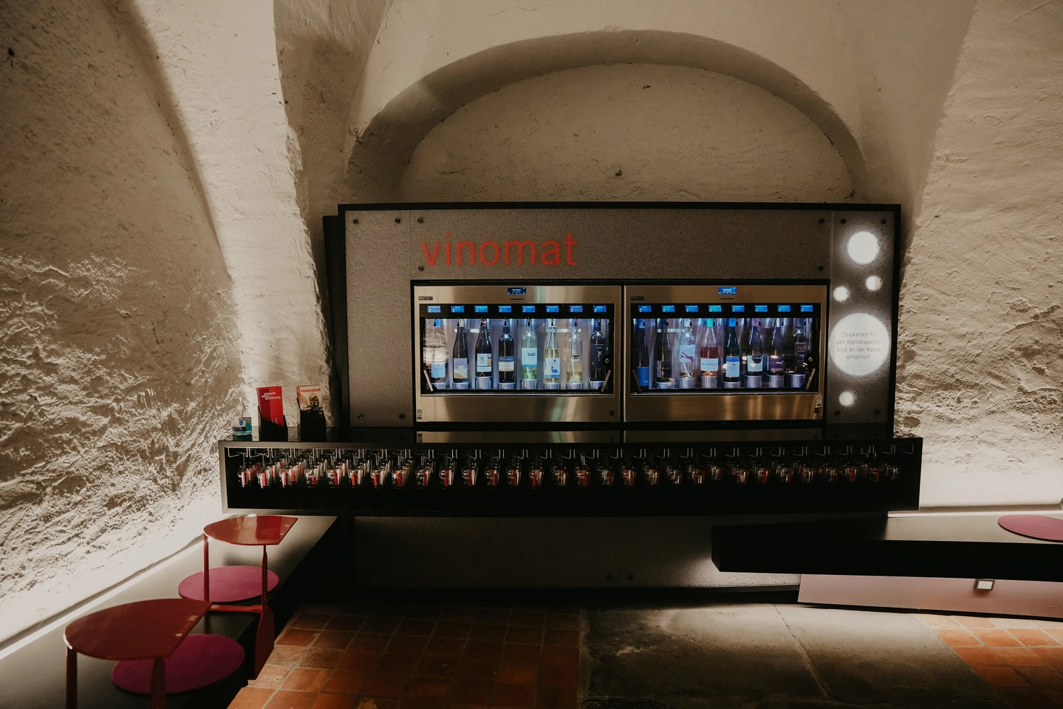 Blick auf einen sylisch beleuchteten Vinomaten in einem großen Gewölbekeller