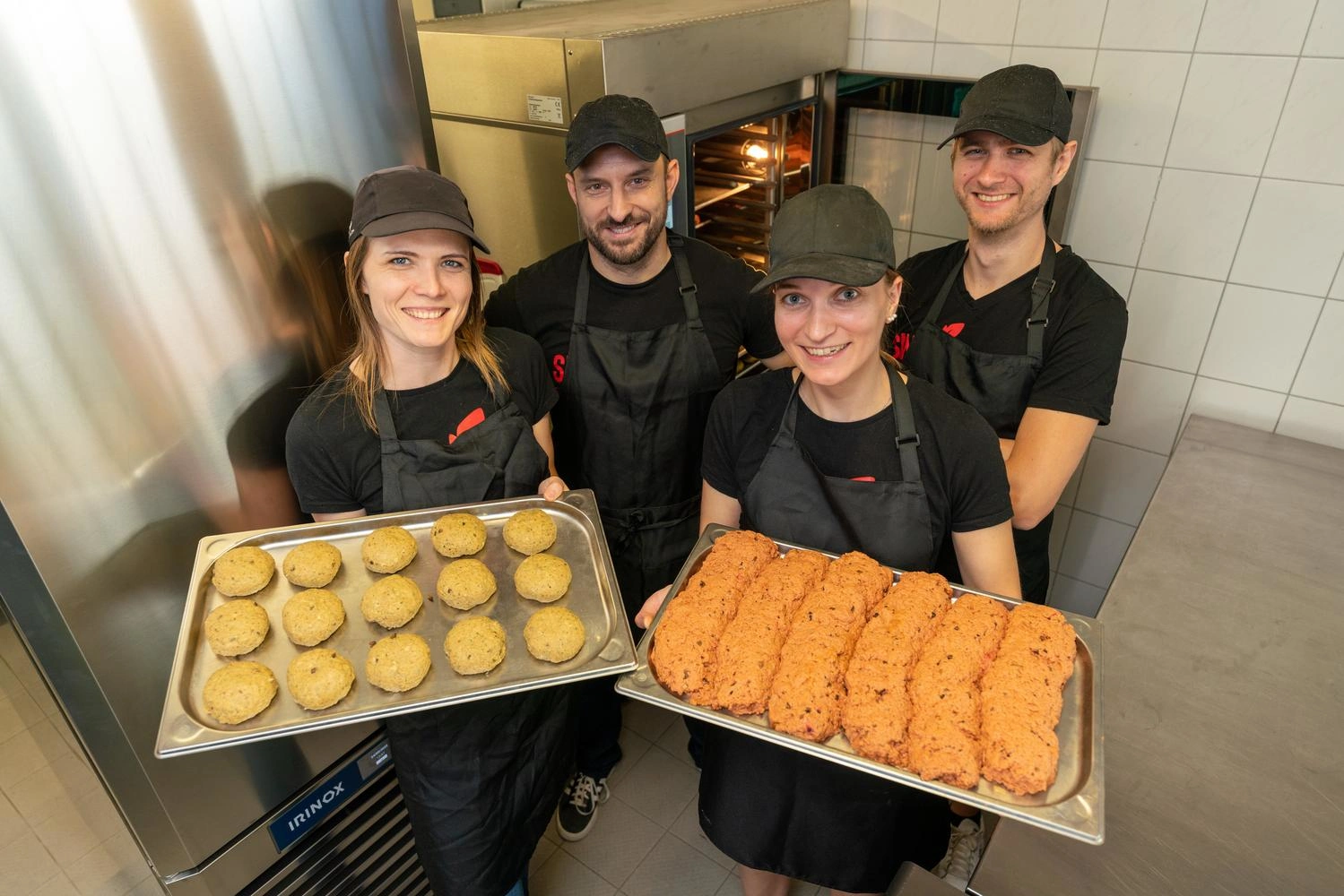 The members of the Freiburg start-up ‘Sin carne’ stand in their kitchen and present two trays of their products.
