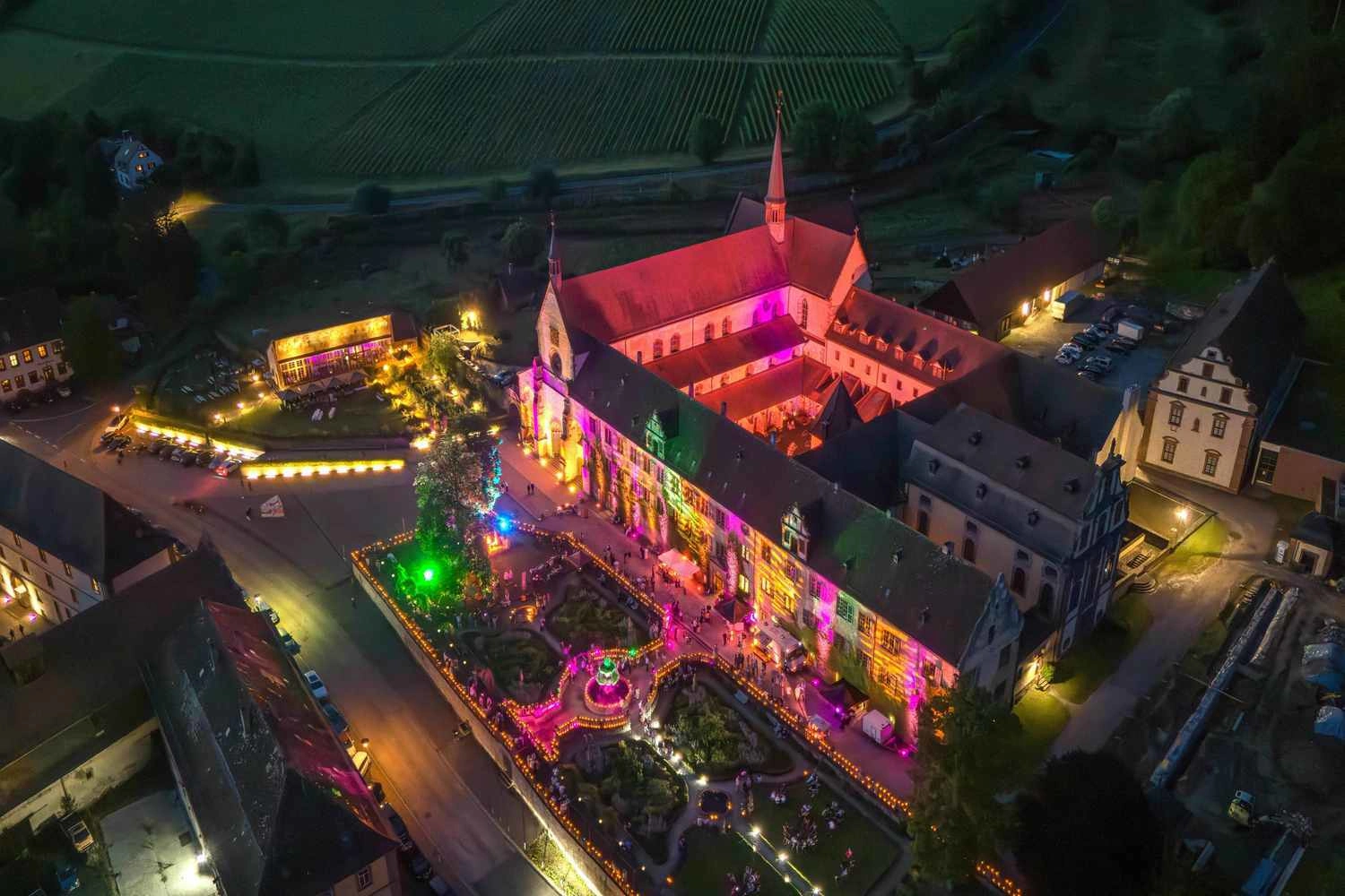 Luftaufnahmen eines Klosters bei Nacht, das mit bunten Lichtern beleuchtet wird. 