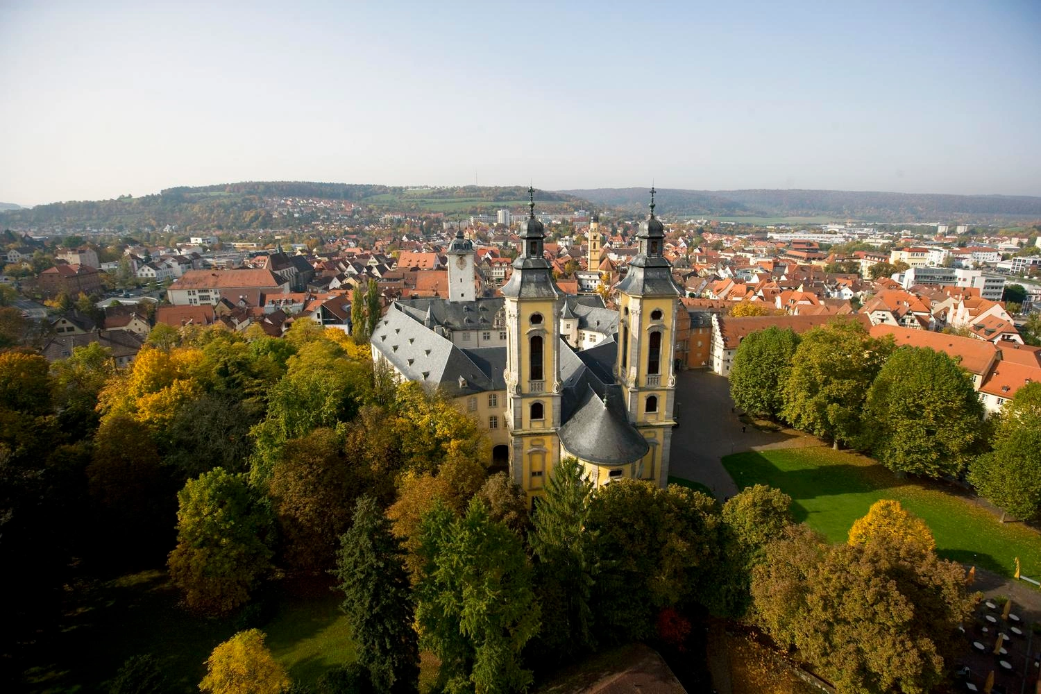 Blick auf ein Schloss, das von Bäumen umgeben ist. Im Hintergrund befindet sich eine Stadt.