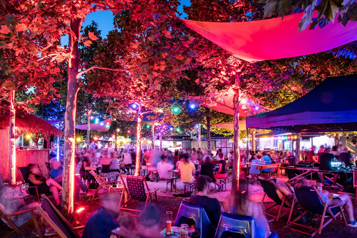 Open-air bar with colorful fairy lights, deck chairs, and lots of guests under the trees; relaxed atmosphere at night, music, and drinks in the Soundgarten at Roxy Ulm.
