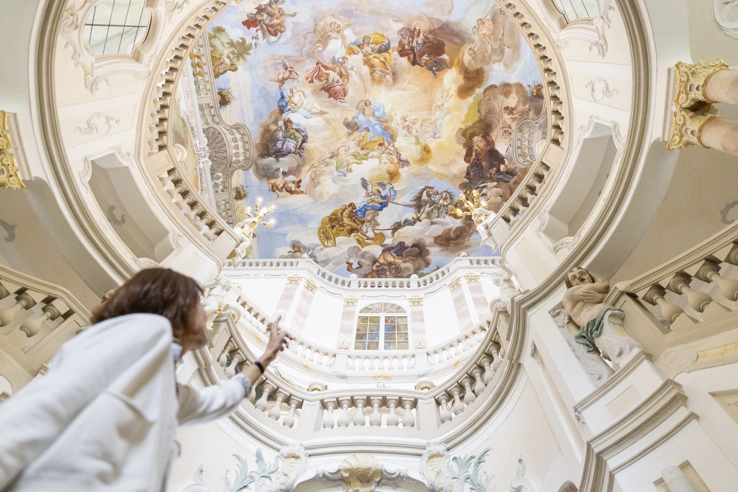 Eine Frau steht in einer impossanten Kuppel mit Barock-Gemälden und schaut nach oben