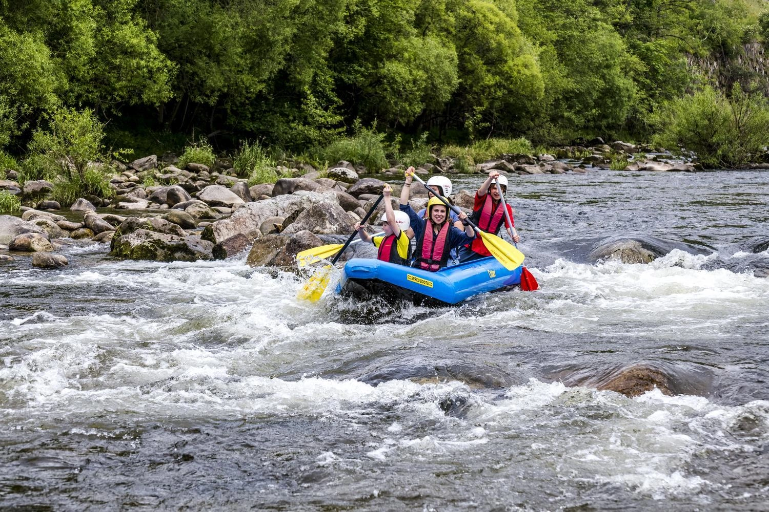 Four people are travelling down a river in a dinghy with a paddle.