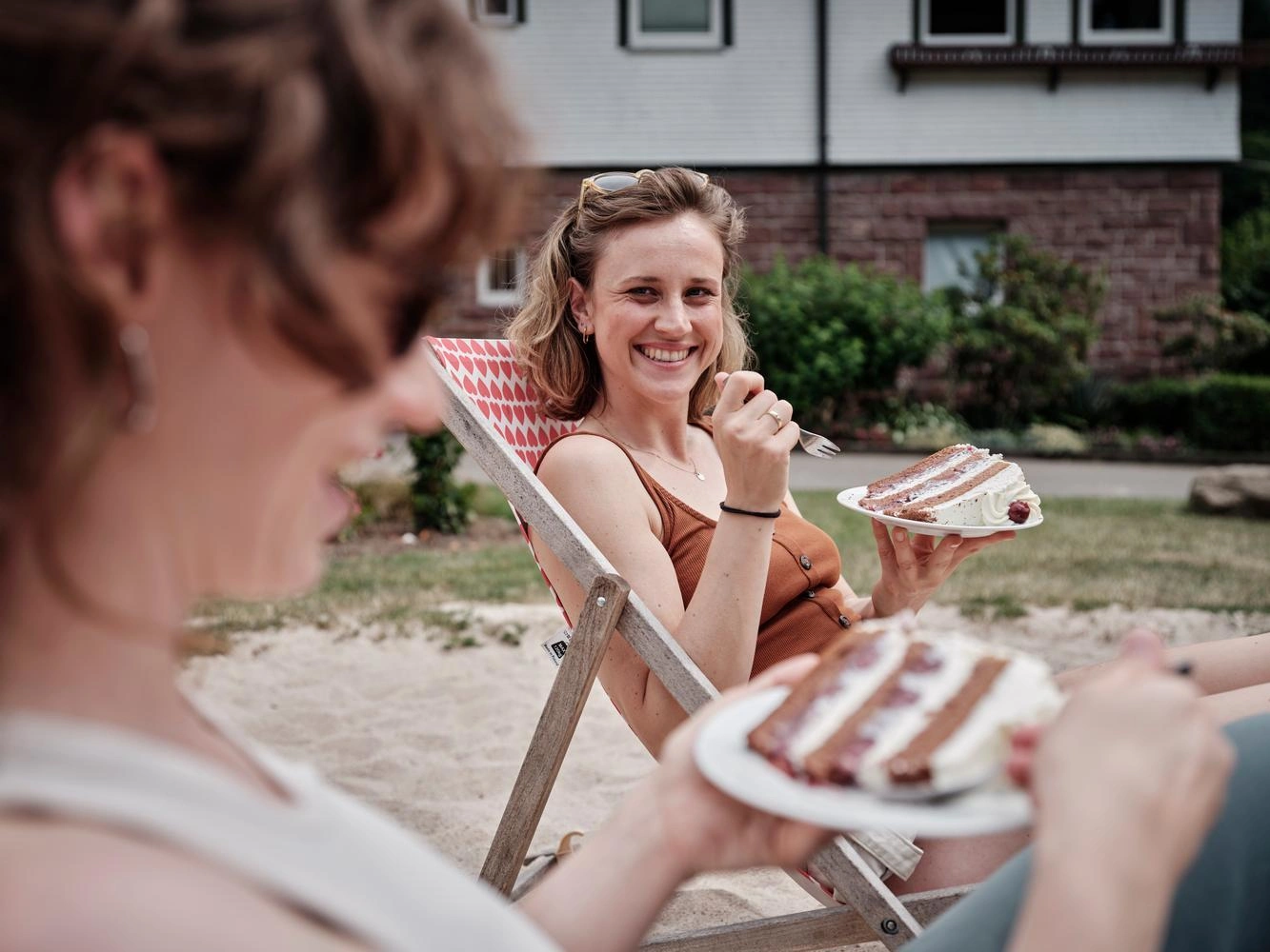 A woman sitting in a deck chair is smiling as she holds a plate with a slice of Black Forest cake.