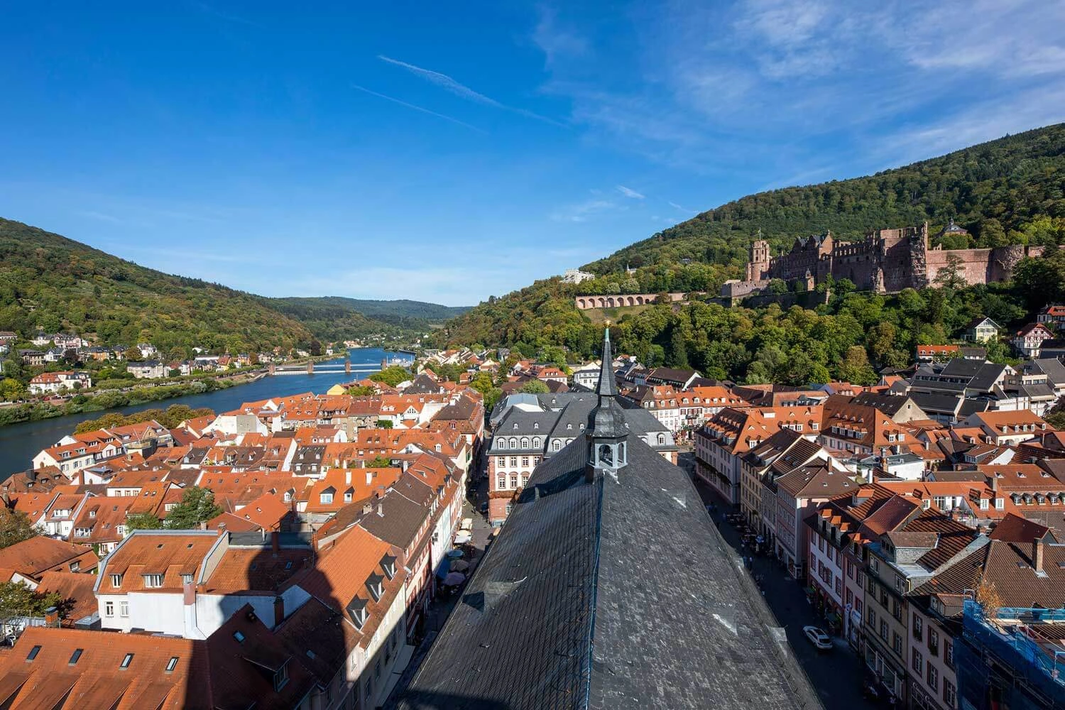 Blick von einem Kirchturm über eine Altstadt. Oberhalb der Stadt befindet sich eine Burgruine.