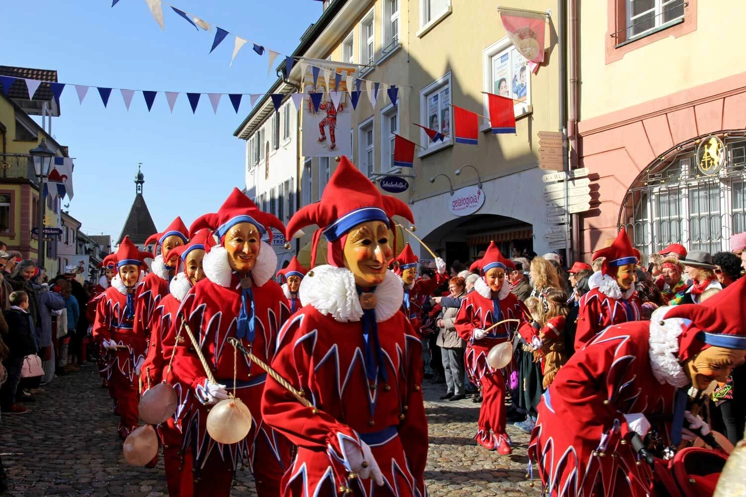Narren ziehen mit Häß durch eine geschmückte Gasse bei schönem Wetter