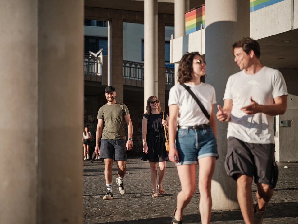 Four people stroll through the city in summer and have a lively conversation.