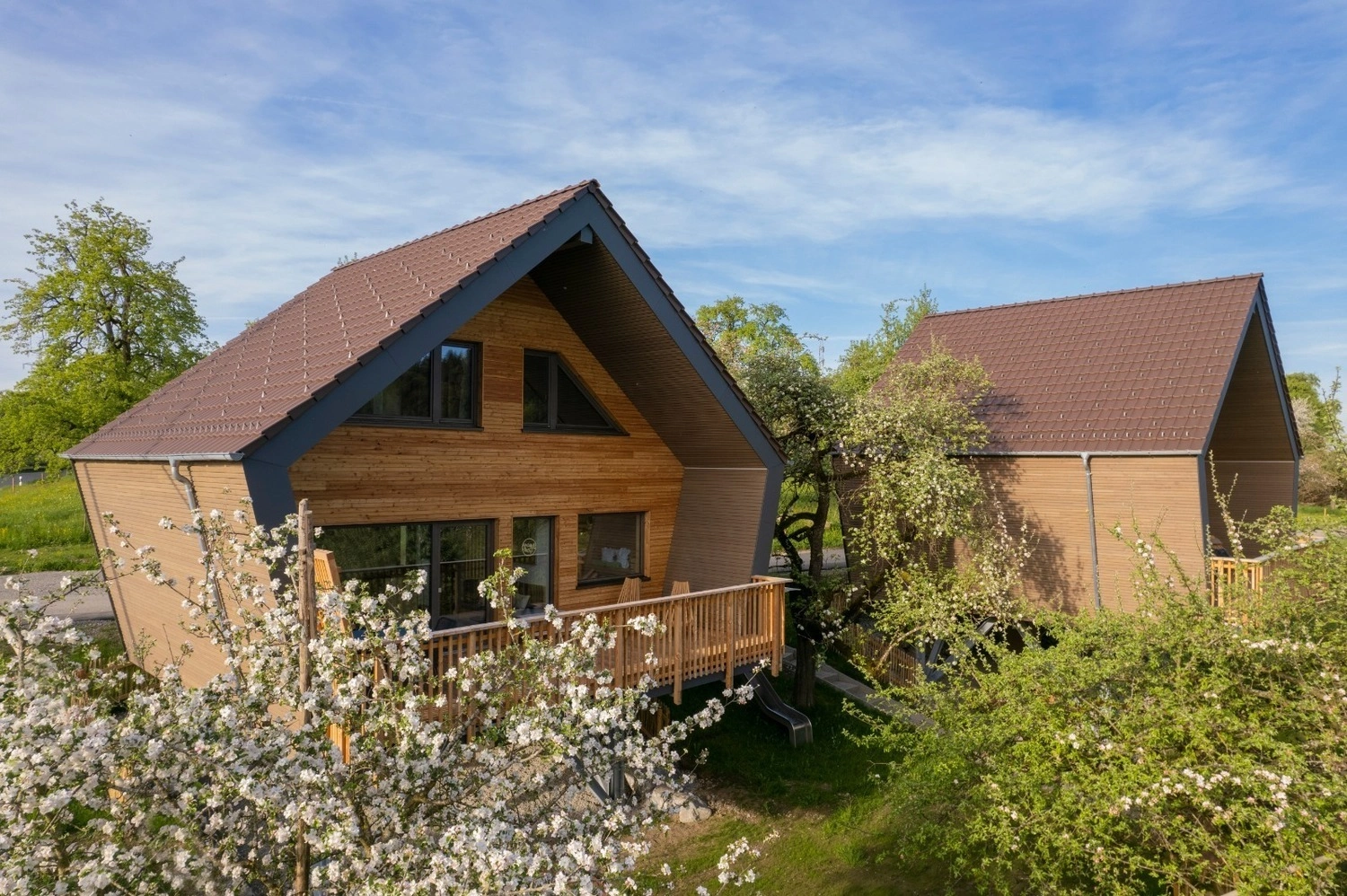 Zwei Chalets, die aussehen wie Baumhäuser, stehen auf einer Streuobstwiese.