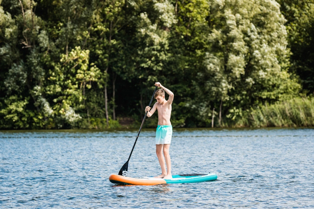 Ein Junge steht auf einem Stand-Up-Paddelboard mitten auf einem See.