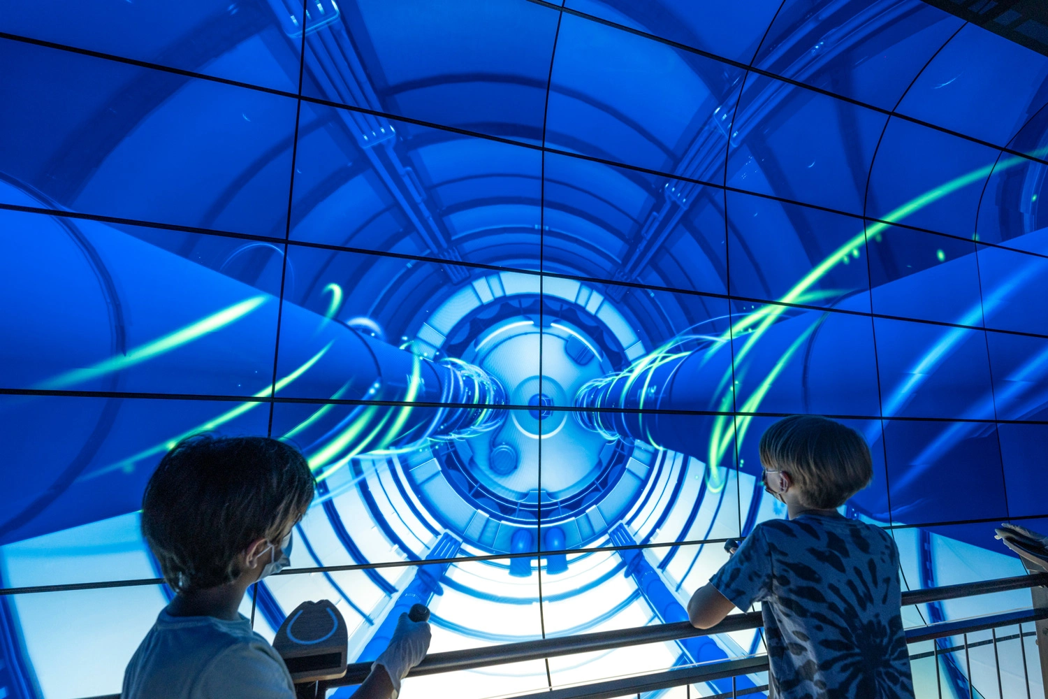  Two children stand in front of a large screen whose content can be controlled with joysticks.