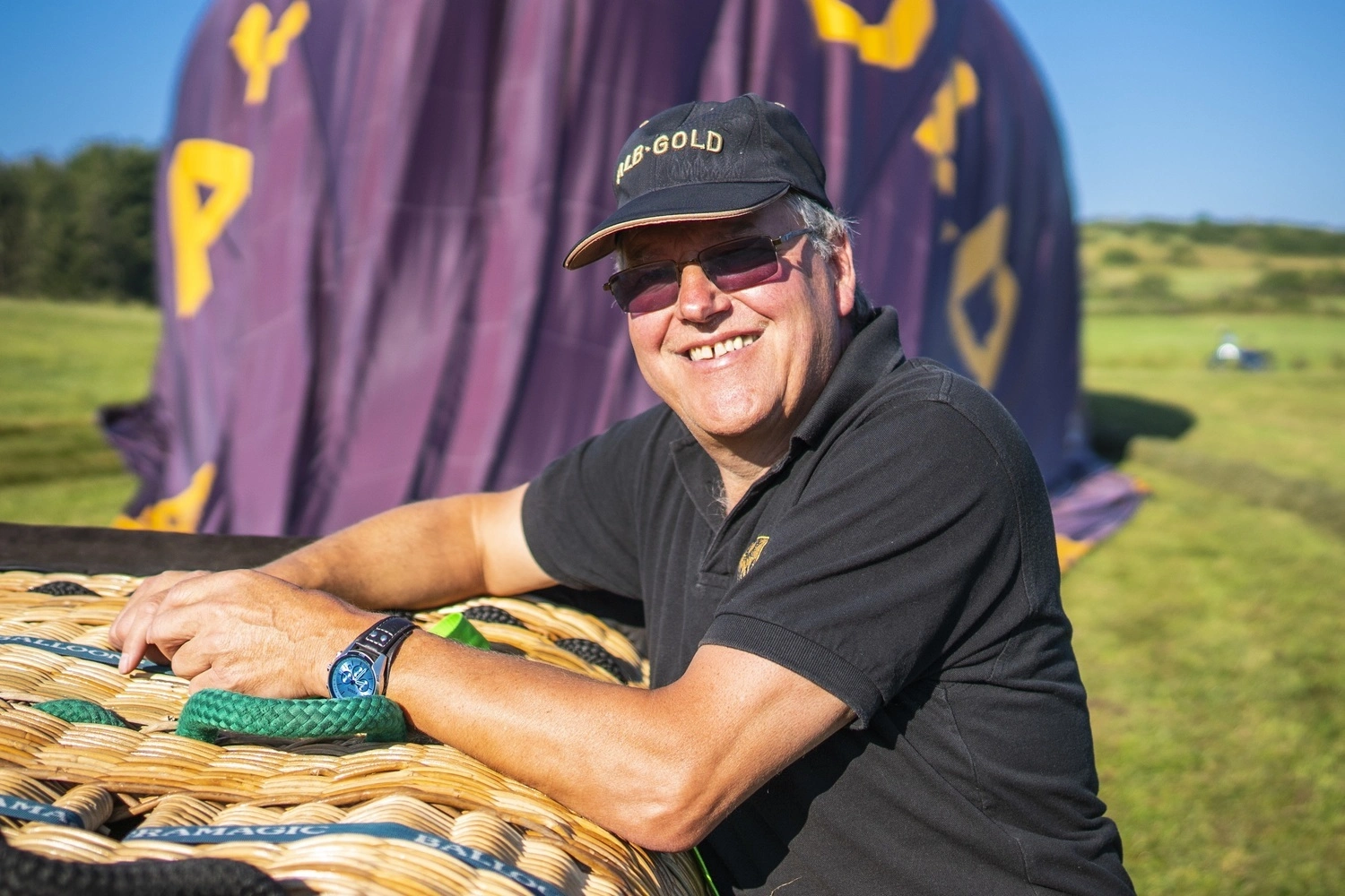 A man is leaning against the basket of a horizontally positioned hot-air balloon.