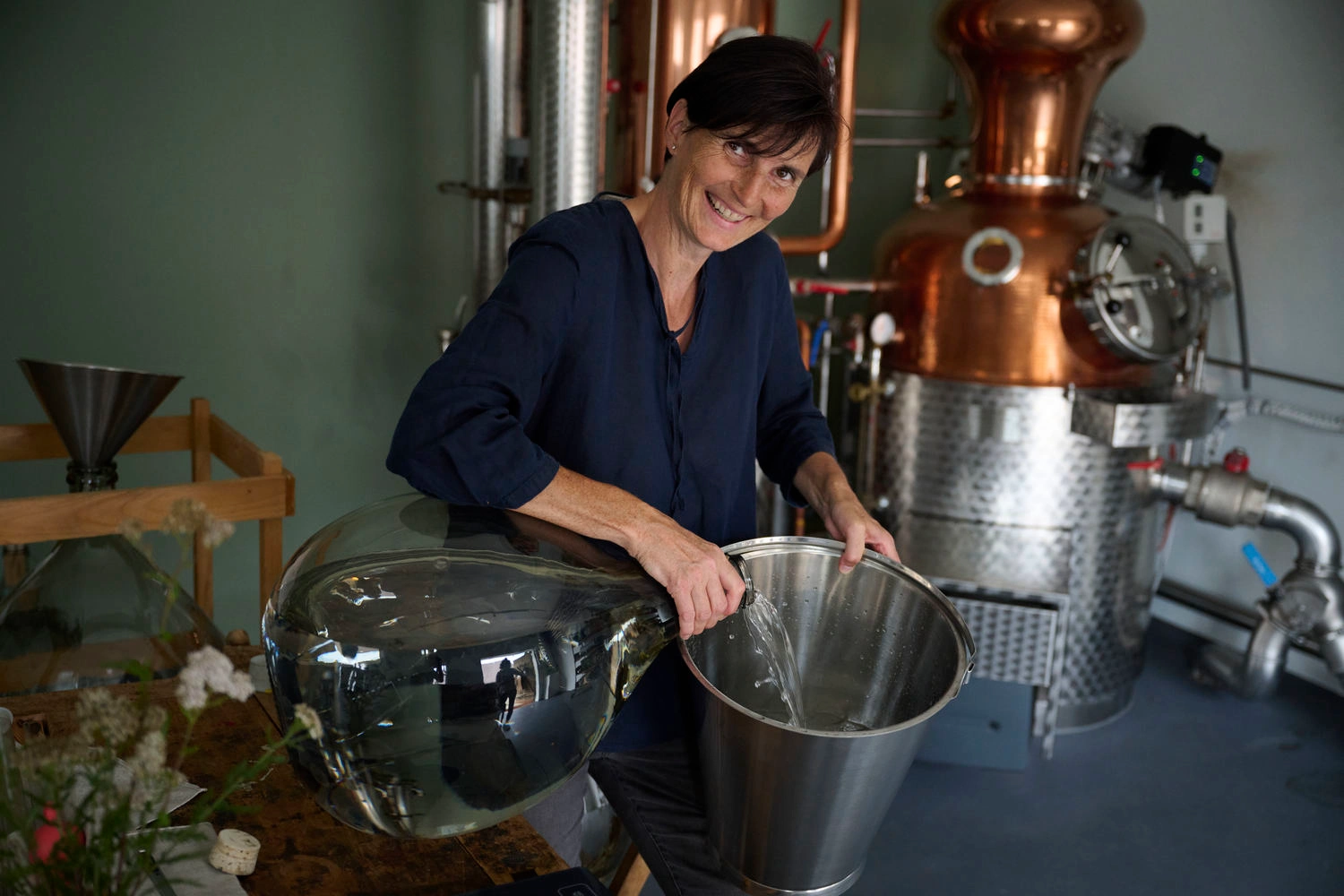 A woman pours a colorless liquid from a carafe into a bucket.