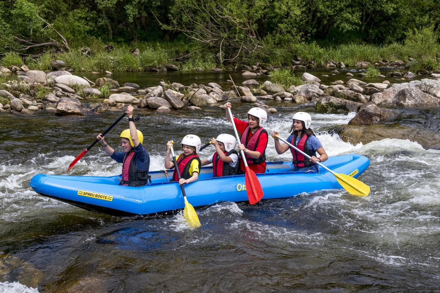 Children and teenagers sit in a boat and raft down a river.