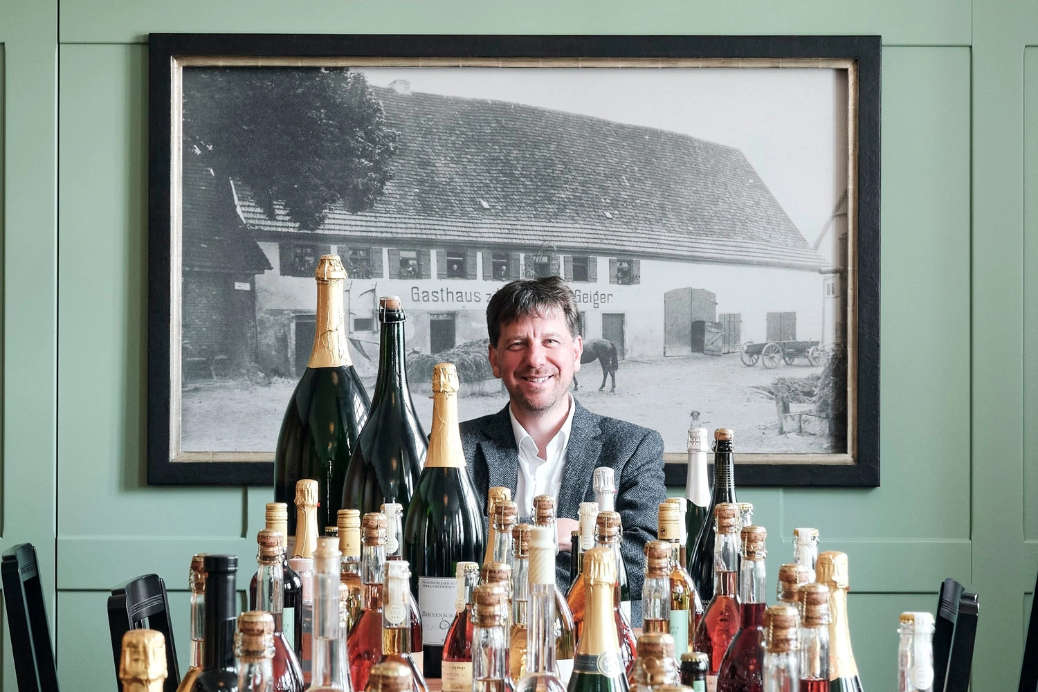 Jörg Geiger with his home-made drinks, which are placed in bottles on a table in front of him.
