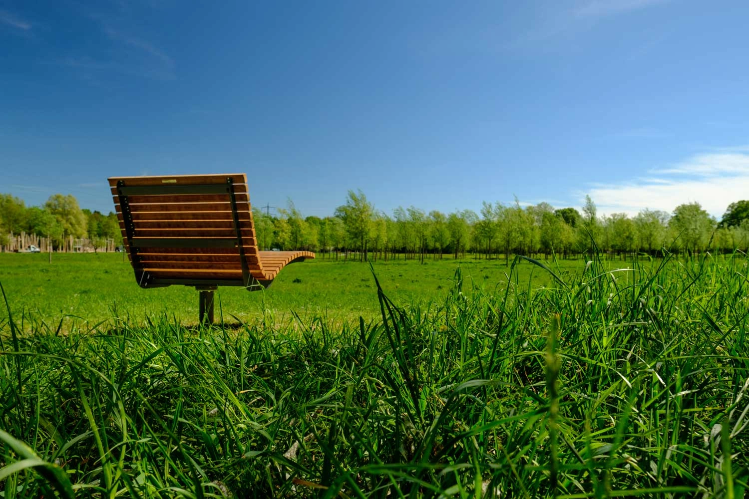 A permanently installed wooden lounger stands in the middle of a green meadow.
