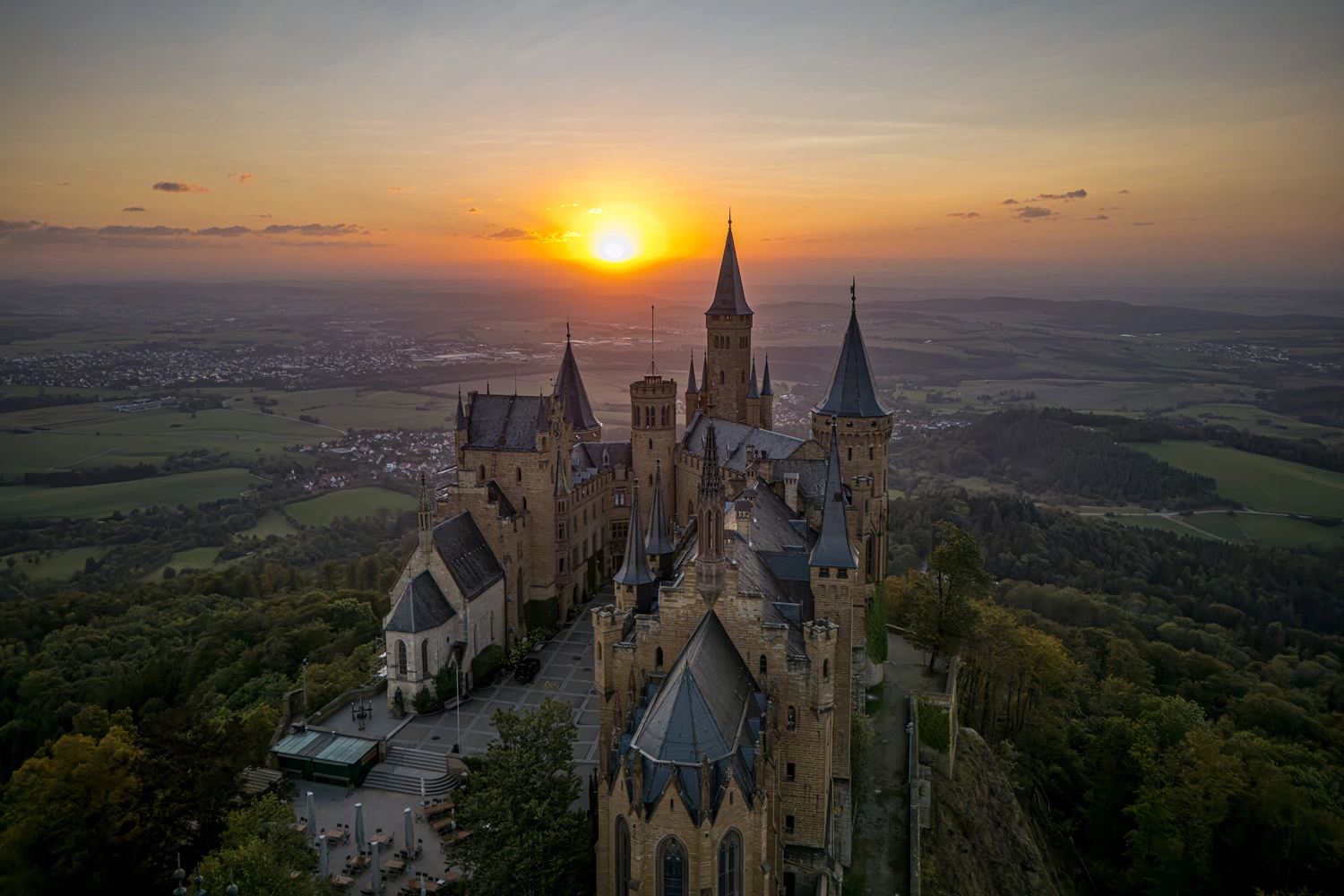 Burg Hohenzollern auf der Schwäbischen Alb im Sonnenuntergang, umgeben von grünen Hügeln und weitem Talblick.