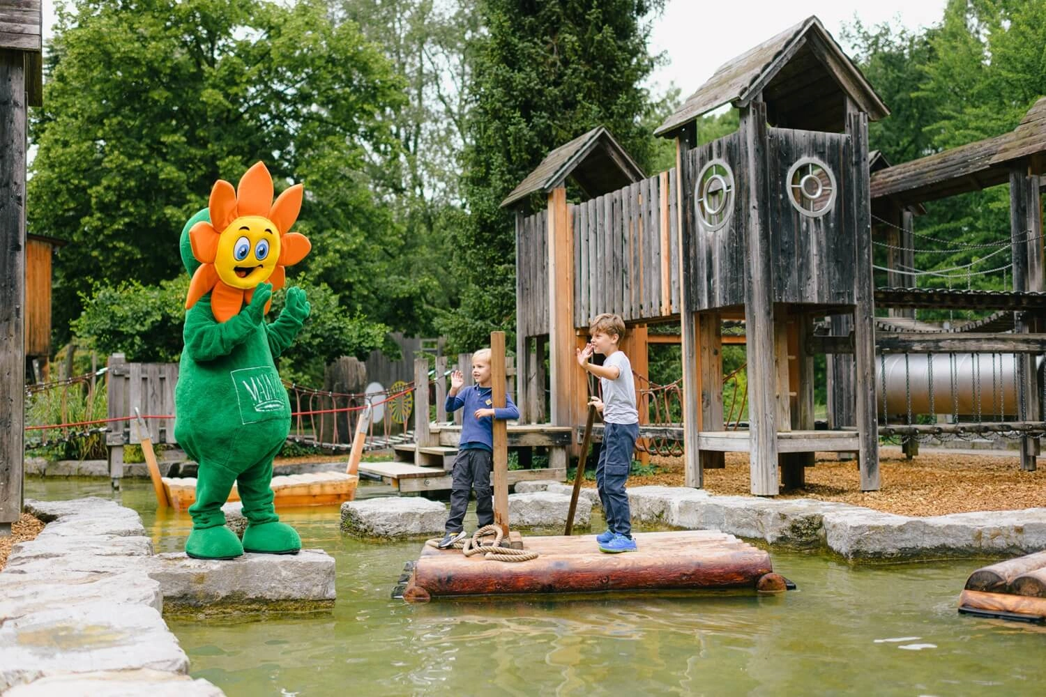 Two children and a flower-shaped mascot at a water playground