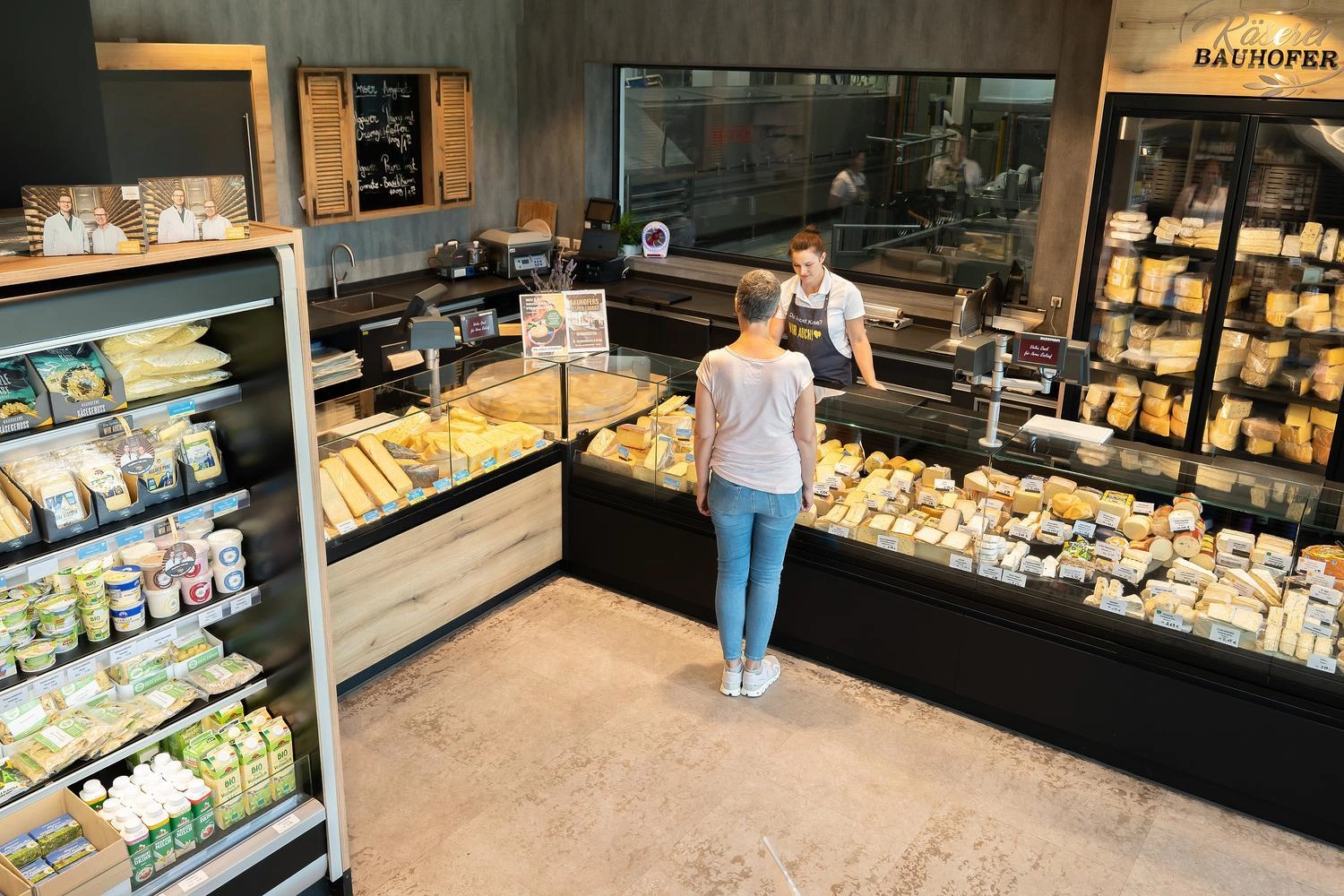 Bedientheke einer Käserei mit großer Auswahl an Käsesorten und Kühlregalen voller regionaler Produkte.