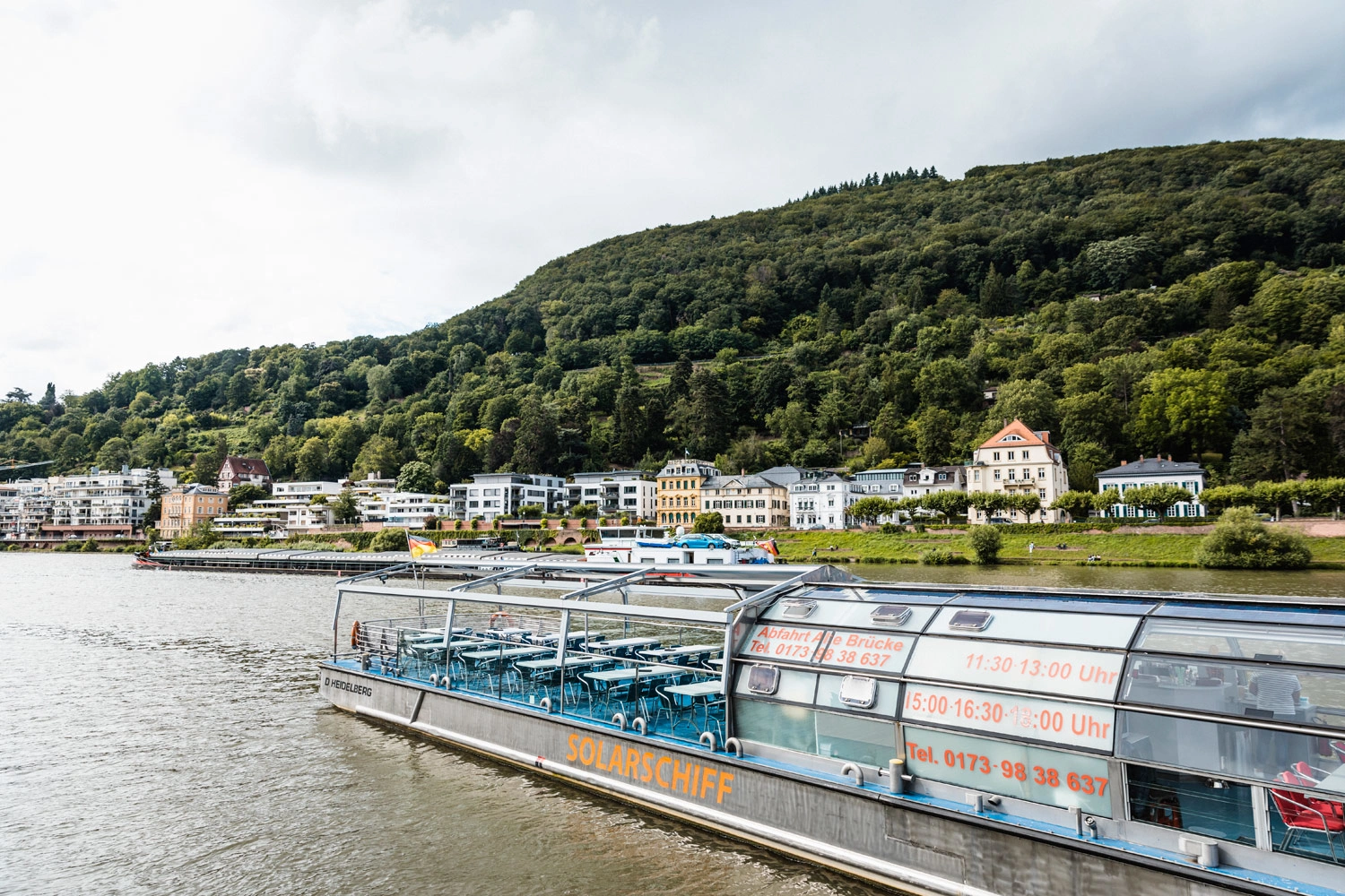 Ein Schiff auf einem Fluss. Im Hintergrund eine Häuserpromenade.