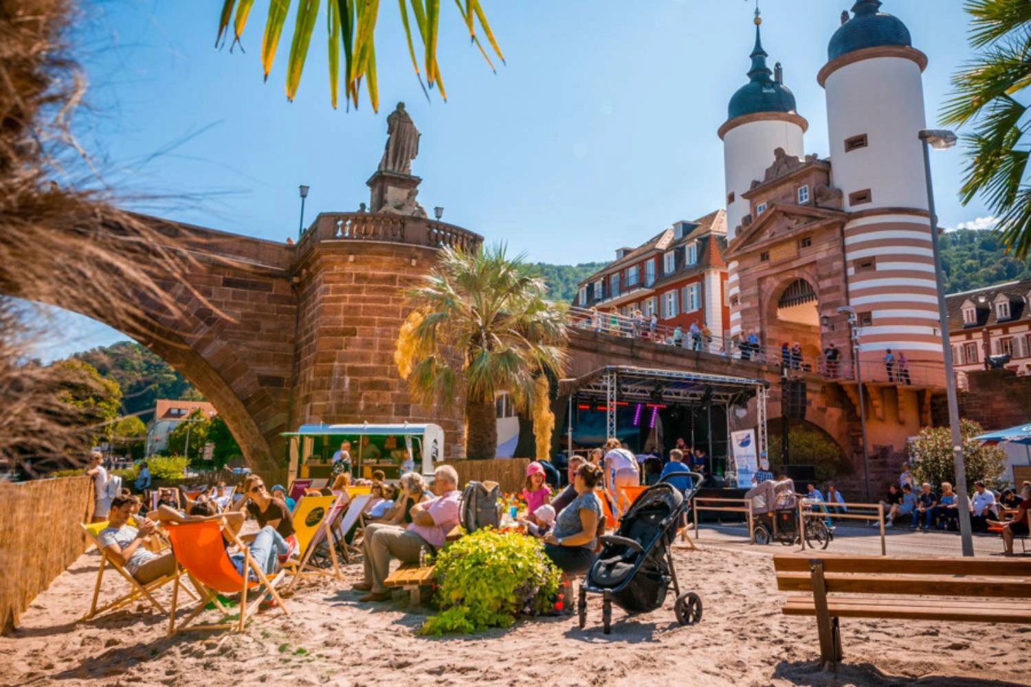 Menschen entspannen auf einem aufgeschütteten Sandstrand in der Altstadt von Heidelberg.