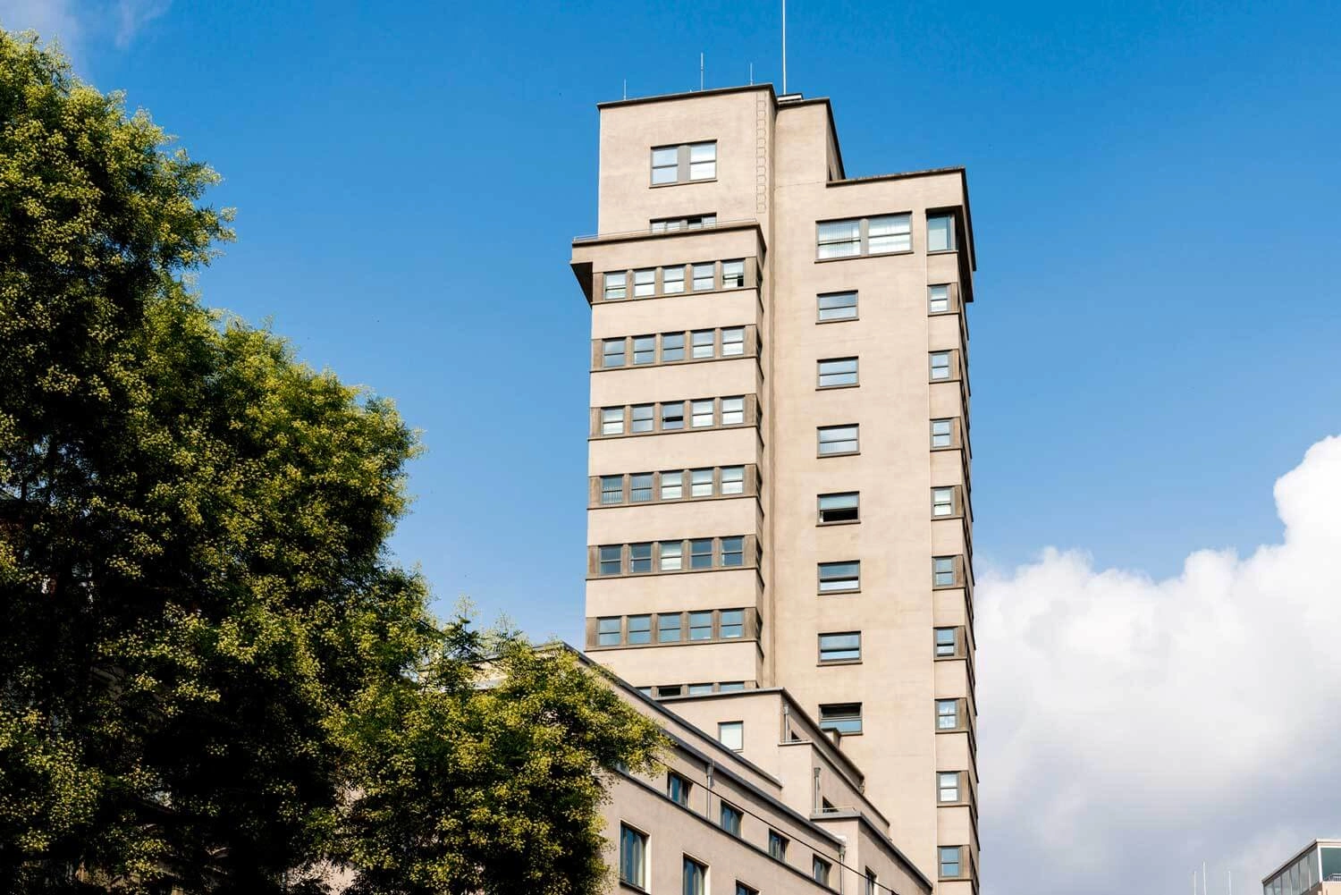 View of the Tagblatt Tower in Stuttgart in exposed concrete construction. Green trees are in the foreground.