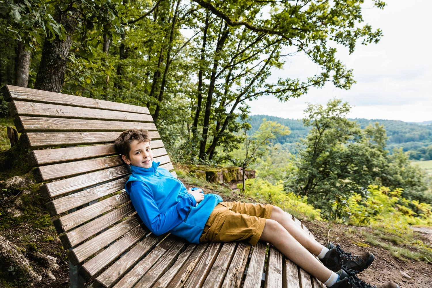 Ein Junge macht eine Pause auf einer Liege am Waldrand mit Panoramablick ins Tal.