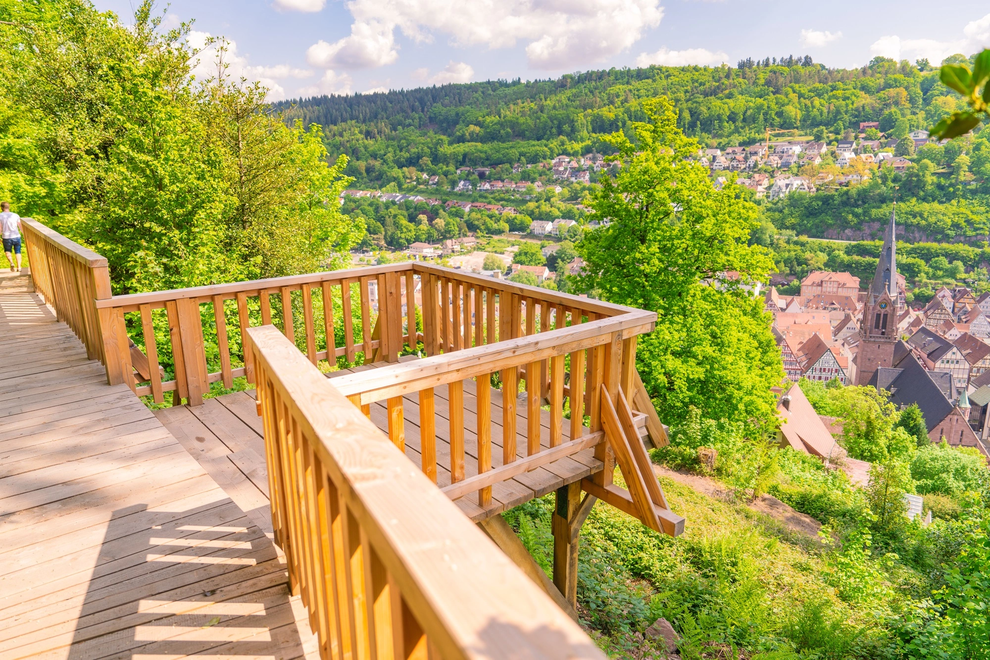Aussichtsplattform mit Holzgeländer über einer Altstadt mit Fachwerkhäusern und Kirchturm, umgeben von bewaldeten Hügeln; zeigt Panorama und Sehenswürdigkeit.