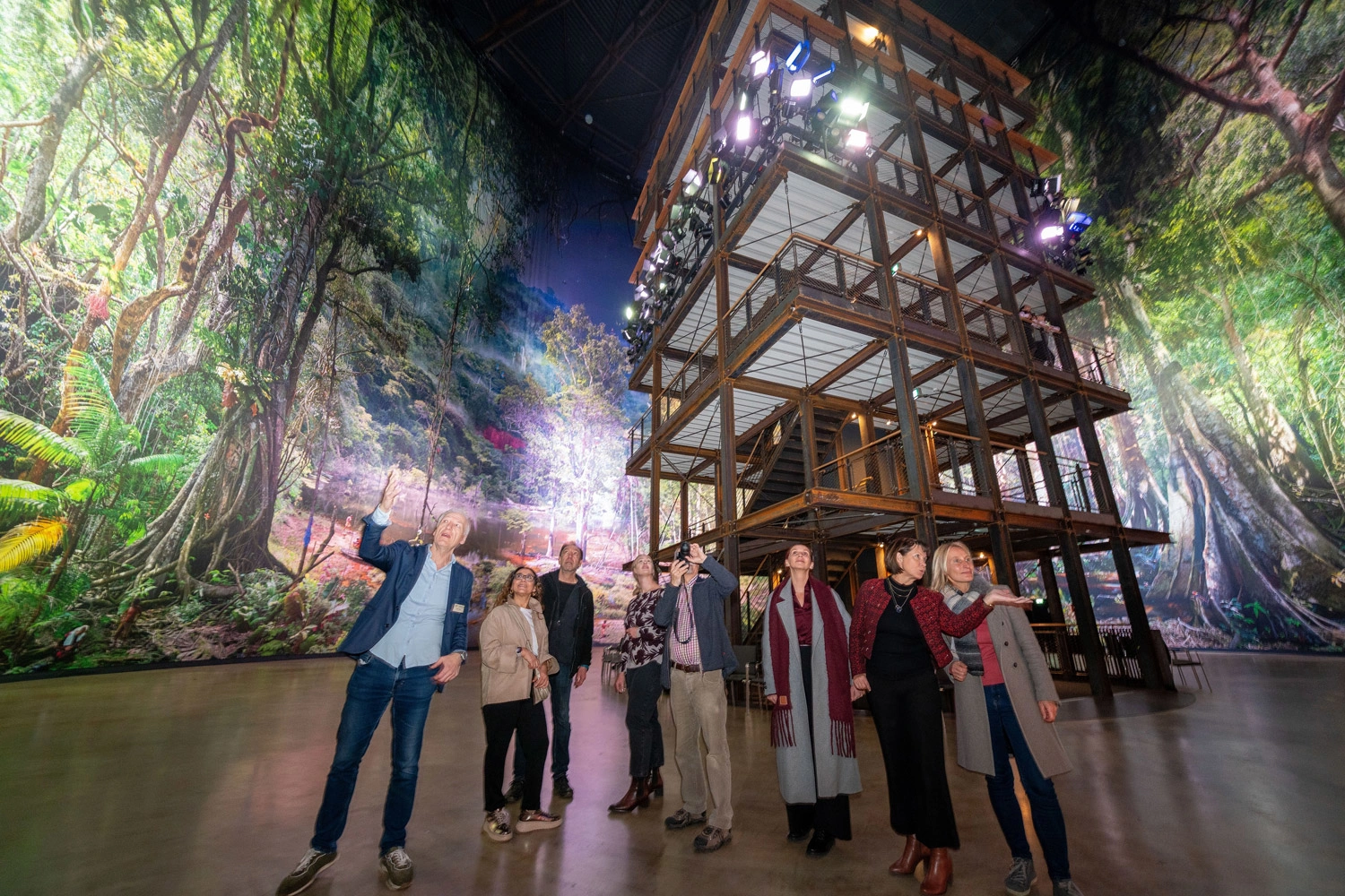 Group on a guided tour of the Pforzheim Gasometer, surrounded by a monumental, detailed panoramic installation with a jungle motif.
