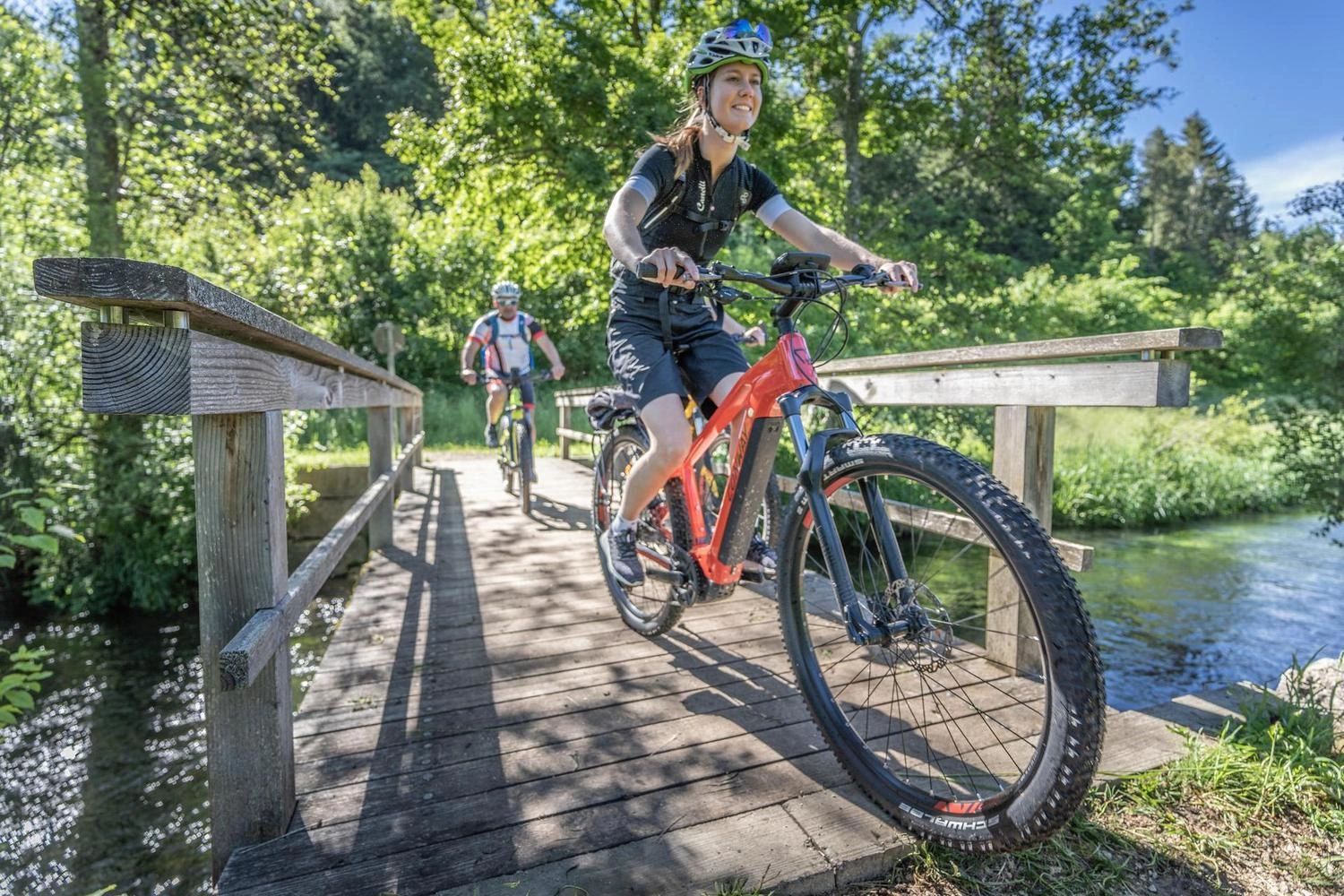 Zwei Radfahrende überqueren auf Fahrrädern eine kleine Holzbrücke über einen Fluss im Großen Lautertal.