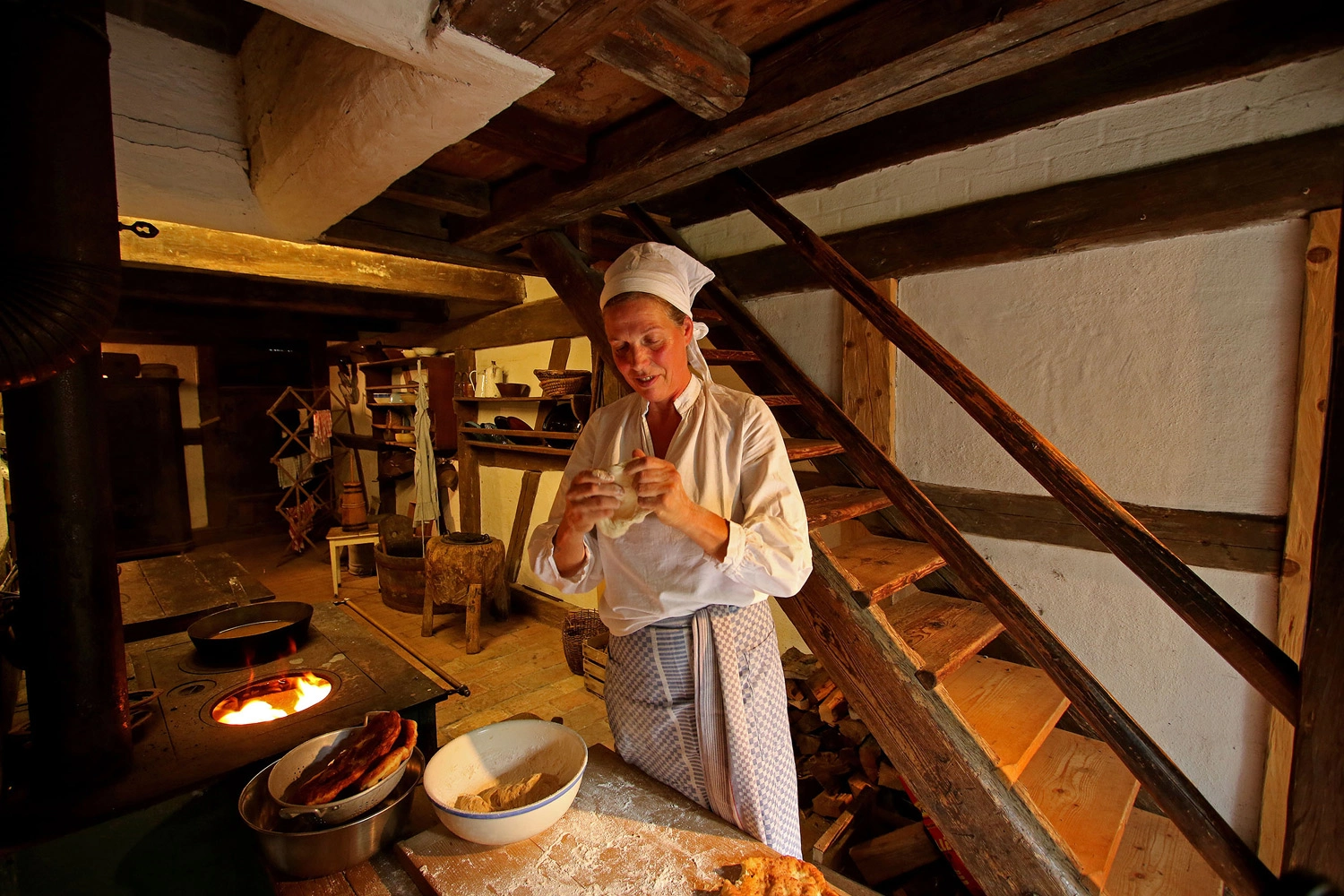 Ein Frau in ländlichem Gewand backt Brot von Hand in einem alten Bauernhaus.