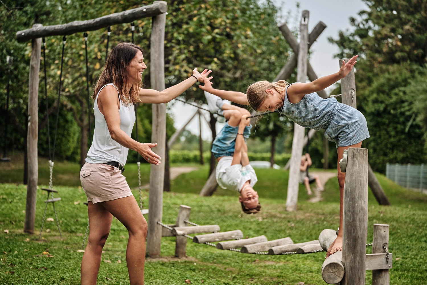 Eine Mutter spielt mir ihren zwei kindern auf einem Spielplatz im Sommer. Die drei sind ausgelassen und haben viel Spaß.
