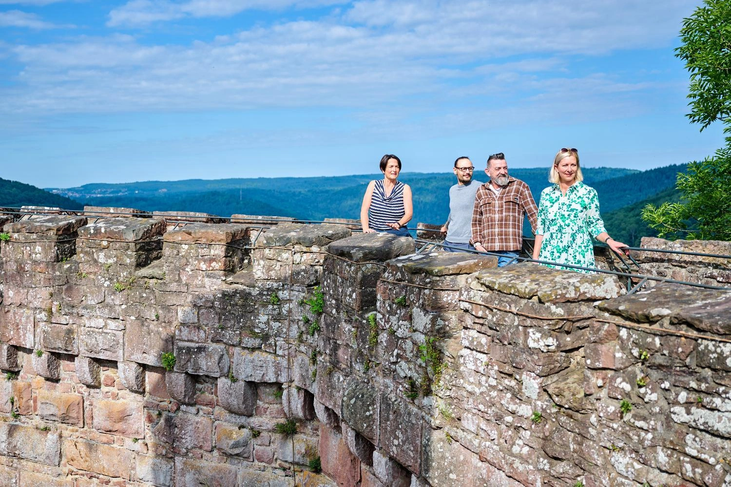 Four people stand on the old castle wall and enjoy the sweeping view over the green hills and blue sky.