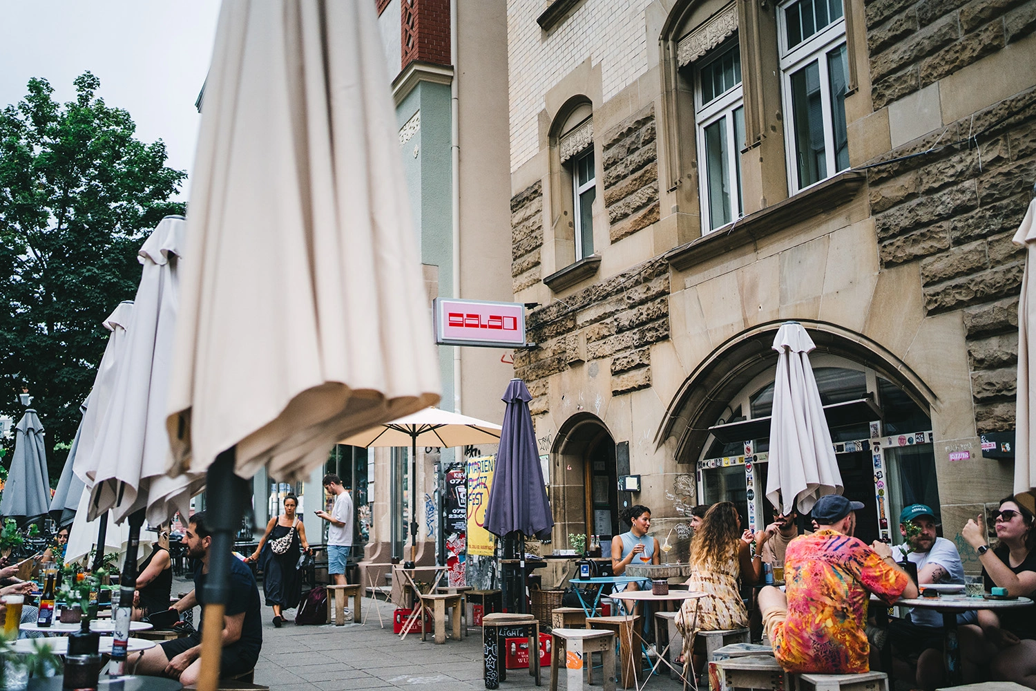 Verzerrte Spiegelung eines belebten Straßencafés mit Gästen, Sonnenschirmen und historischer Hausfassade.