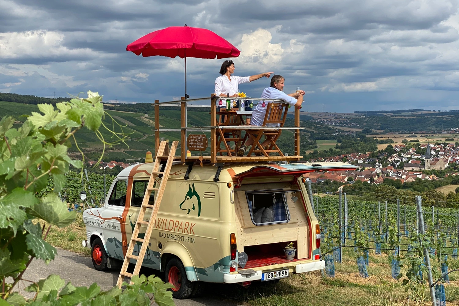 Ein Paar sitzt auf der Dachterasse eines kleinen Busses und blickt in die Weinberge.