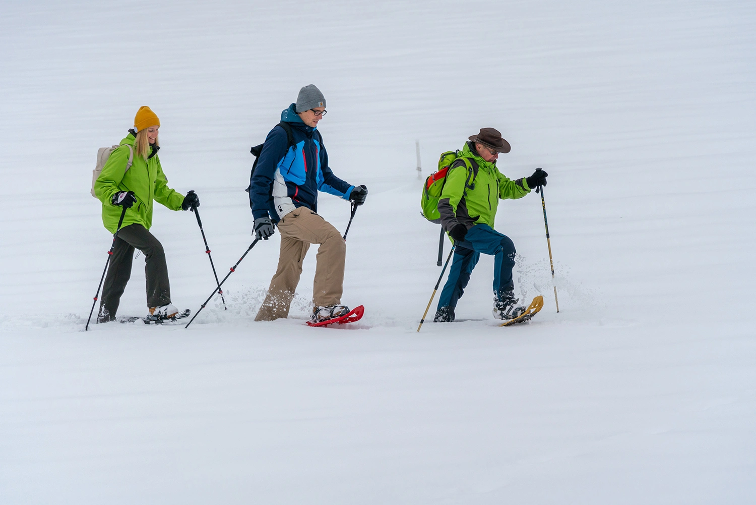 People in a row snowshoeing through thick snow.