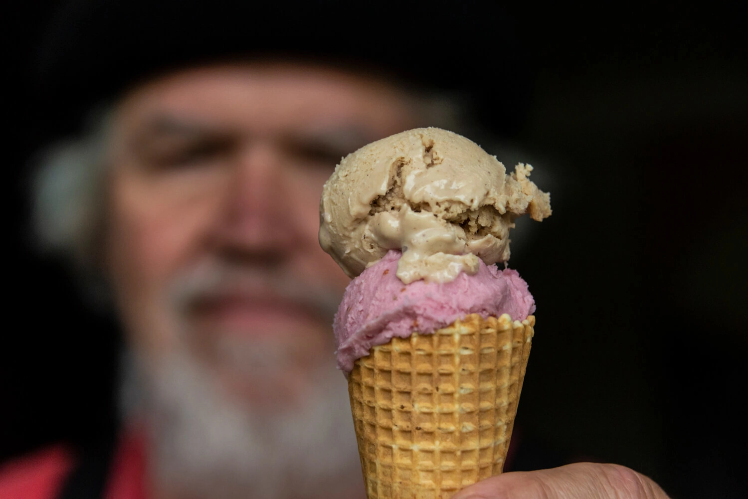 A man is holding an ice cream cone with two scoops of ice cream inside.