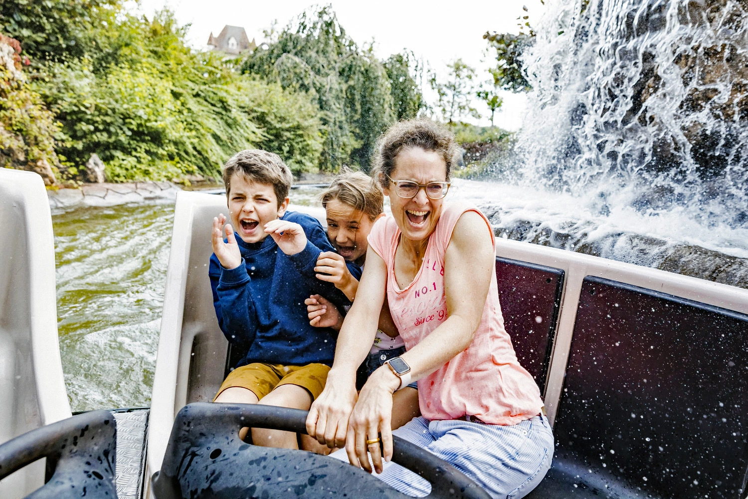 A woman with two children sits happily in a rafting tube and is splashed with water.
