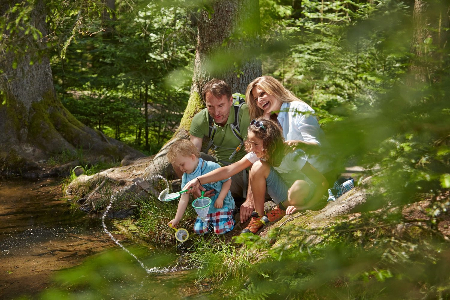 A family is splashing around in a pond in the woods.
