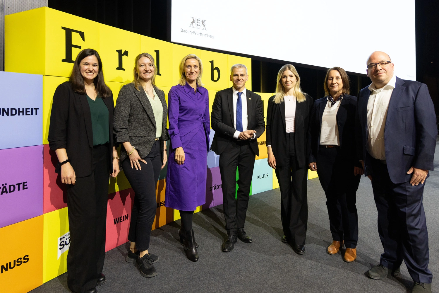 7 Personen stehen in einem geschäftlichen Kontext in einem Halbkreis